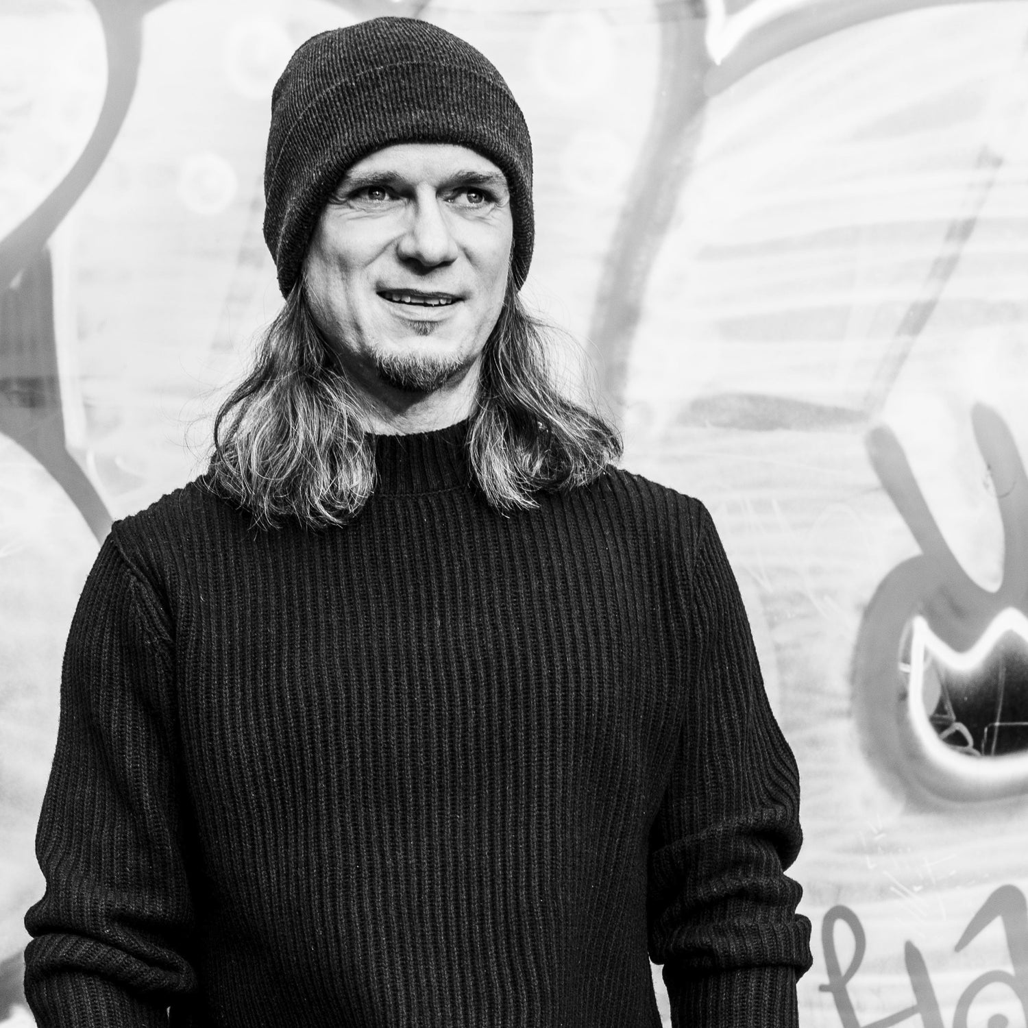 Schwarz-Weiß Portrait von Thomas Godoj im Strickpullover mit Mütze vor einer Graffiti-Wand